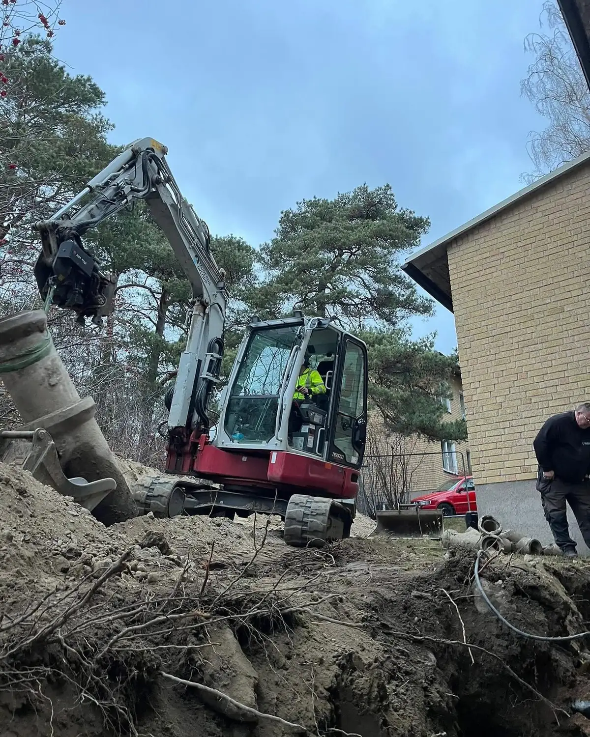 Grävmaskin utför dräneringsarbete runt husgrund i Stockholm